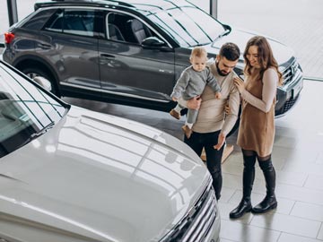 Eine Familie erkundet bei Autoankauf Lüneburg und bewundert ein weißes Fahrzeug, während ein stilvoller SUV im Hintergrund in einem modernen Showroom zu sehen ist.